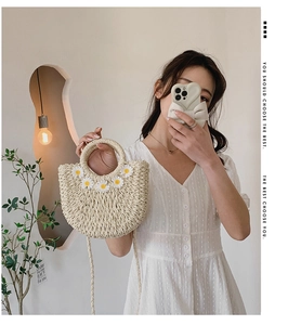 Detail view of woven straw bag featuring white daisy embroidery and round handle