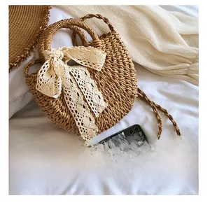 Size comparison of summer straw round handbag with lace bow showing hand and crossbody straps