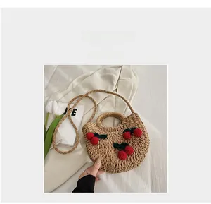 Close-up of woven straw handbag featuring red crochet cherries and circular handles