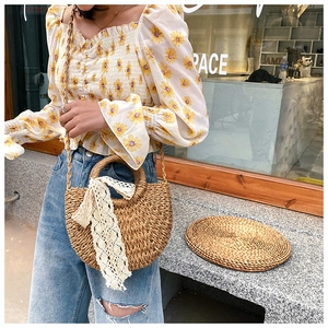 Straw half-moon crossbody bag featuring a large white lace bow and woven shoulder strap
