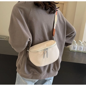 Détail d'un sac bandoulière beige avec sangle brodée colorée porté par un modèle