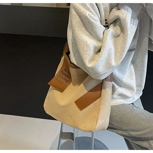 Detail view of large canvas crossbody bag featuring brown leather trim and side label