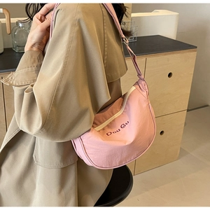 Détail du sac croissant rose en nylon avec broderie porté par un mannequin en trench