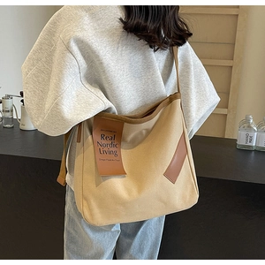 Detail view of a large beige canvas shoulder bag with brown leather straps and accents