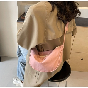 Sac bandoulière rose en forme de croissant porté avec un trench-coat décontracté