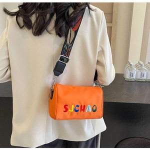 Détail d'un sac bandoulière orange en nylon avec broderie et sangle ethnique