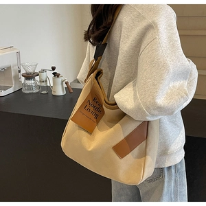 Close-up of beige canvas crossbody bag with brown leather accents and wide strap