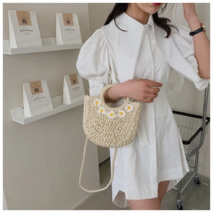 Detail of woven straw crossbody bag with white daisy floral accents and braided strap