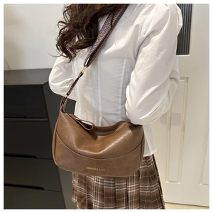 Close-up of brown crescent crossbody bag with patterned strap and golden logo detail