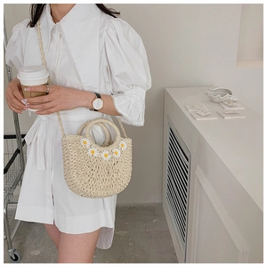 Detailed close-up of woven beige straw bag with white daisy floral appliques and handle
