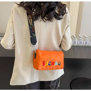 Détail du sac cylindrique orange avec broderie SJCHAO colorée et bandoulière à fleurs