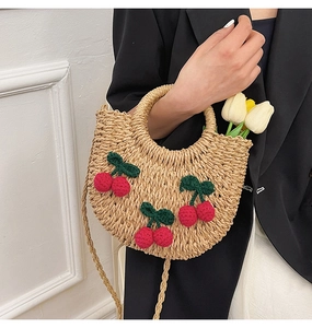 Detail of woven straw crescent handbag featuring handmade crochet cherry accents and long strap