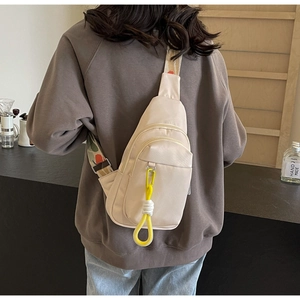 Detail of a creamy white nylon crossbody bag with colorful woven strap and yellow cord accent