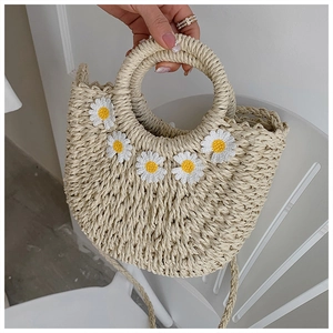 Detail of woven straw crossbody bag featuring white daisy appliques and rounded top handle