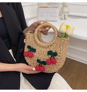 Close-up of a woven straw handbag featuring red crochet cherry accents and round handle