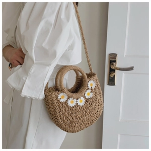 Detailed view of hand-woven straw bag with white daisy floral accents and circular handles