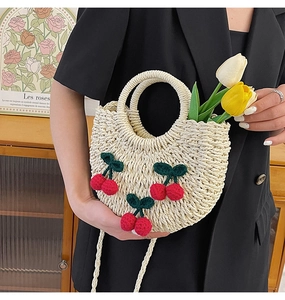 Detail showing hand-woven straw handbag with 3D crochet cherry accents and round handle