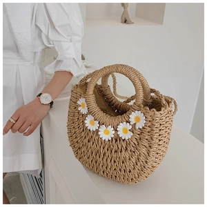 Detail of woven straw handbag featuring delicate white daisy appliques and round handles