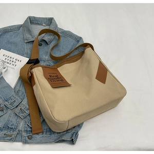 Minimalist beige canvas crossbody bag with brown wide strap on blue denim jacket