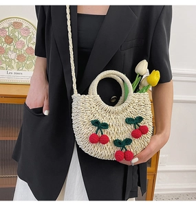 Detail of woven straw handbag with handmade crochet cherries and long shoulder strap