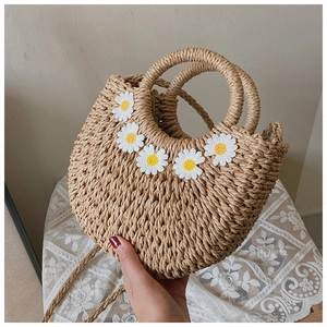 Close-up of hand-woven straw handbag featuring white daisy floral appliques and a round handle