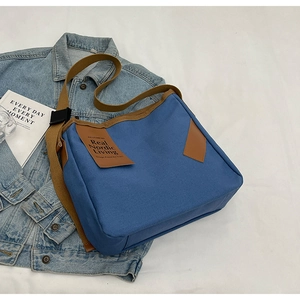 Fashionable blue canvas crossbody bag with brown straps for minimalist spring outfits