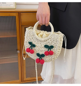 Detail of woven straw handbag featuring red cherry charms and drawstring inner bag