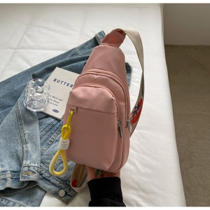Pink nylon crossbody bag with floral strap and yellow tassel accessory on white bedding
