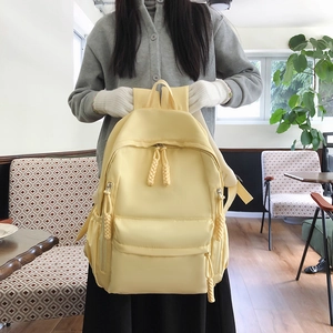 Close-up of cream yellow nylon backpack featuring woven zipper pulls and matte texture