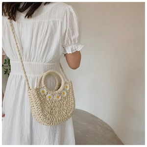 Detailed texture of woven straw handbag featuring delicate white daisy floral embroidery