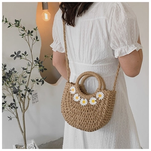 Detail of a woven straw handbag with white daisy ornaments worn by a model in soft lighting