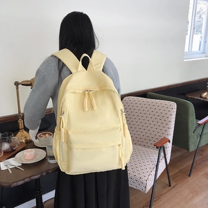 Detail of light yellow nylon backpack with long woven zippers and side elastic pockets