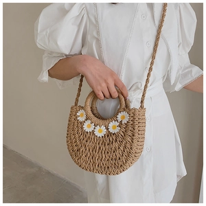 Detail of woven straw handbag featuring delicate white daisy appliques and textured finish