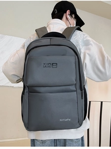 Detailed back view of a dark grey nylon backpack worn by a model in a minimal setting
