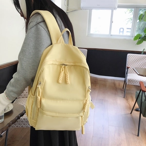 Detail of a light yellow nylon backpack showing woven rope zippers and side pockets