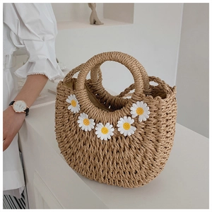 Detailed view of woven straw handbag featuring delicate white daisy embroidery