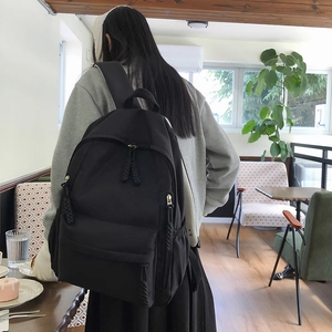 Detail of minimalist black nylon backpack with braided zipper puller in a cafe setting