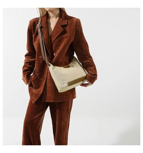 Detail of beige nylon crossbody bag with brown leather trim worn by a model in a corduroy blazer