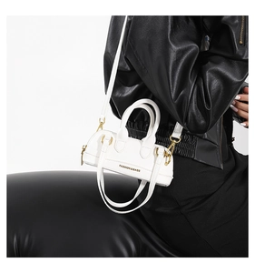 Close-up of white PU leather crossbody bag with gold hardware on a black jacket background