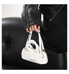 Close-up of a white mini crescent bag featuring gold hardware and logo on a black background