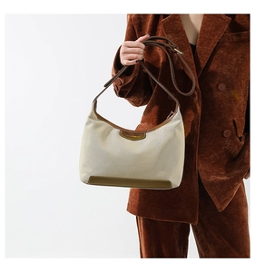 Detail of canvas shoulder bag with brown leather trim held by model in velvet blazer