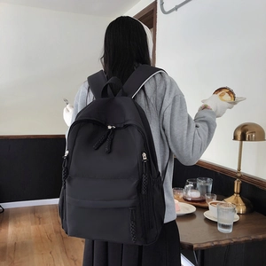 Close-up of a minimalist black nylon backpack with decorative braided rope zipper pulls
