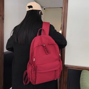 Detail of dark red nylon backpack showing woven rope zipper pulls and side pocket features