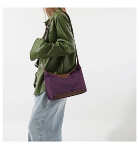 Detail of purple nylon crescent bag with brown leather trim worn by model in a green top
