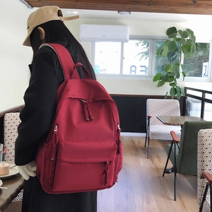 Detail of burgundy nylon backpack featuring woven zipper pulls and side pocket shown on model