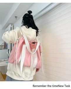 Rear view of a pink canvas drawstring backpack with wide white straps on a female model