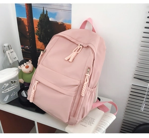 Close-up of a light pink nylon backpack featuring woven rope zipper pull details