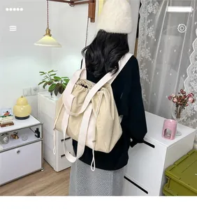 Detail of a beige drawstring backpack with wide textile straps in a cozy home setting