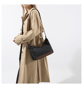 Detail view of black nylon shoulder bag with brown leather trim and golden metal logo brand