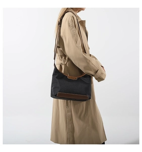 Side view of a black nylon shoulder bag with brown leather trim on a beige trench coat